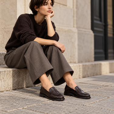 Mocassins artisanaux Billi bi en cuir noir portés par une femme assise sur des marches en pierre
