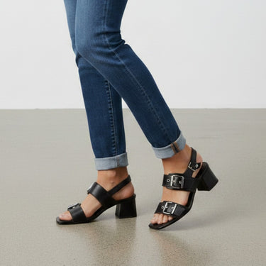 Billi Bi black leather sandals with double buckle straps and block heel, worn with cuffed blue denim jeans.