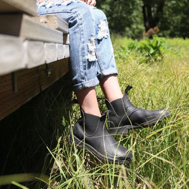 Boots Chelsea Blundstone 558 noires en cuir gras portées avec un jean déchiré dans l'herbe par moodeshop