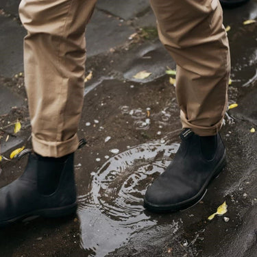 Bottines Chelsea Blundstone 587 en cuir vieilli noir rustique portées avec un pantalon beige dans une flaque d'eau