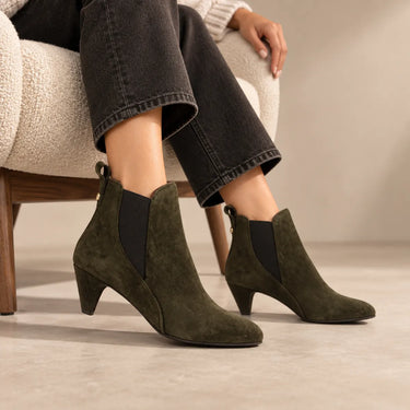 Femme portant les Chelsea boots Rikley en suède vert mousse, assise dans un fauteuil designer moderne